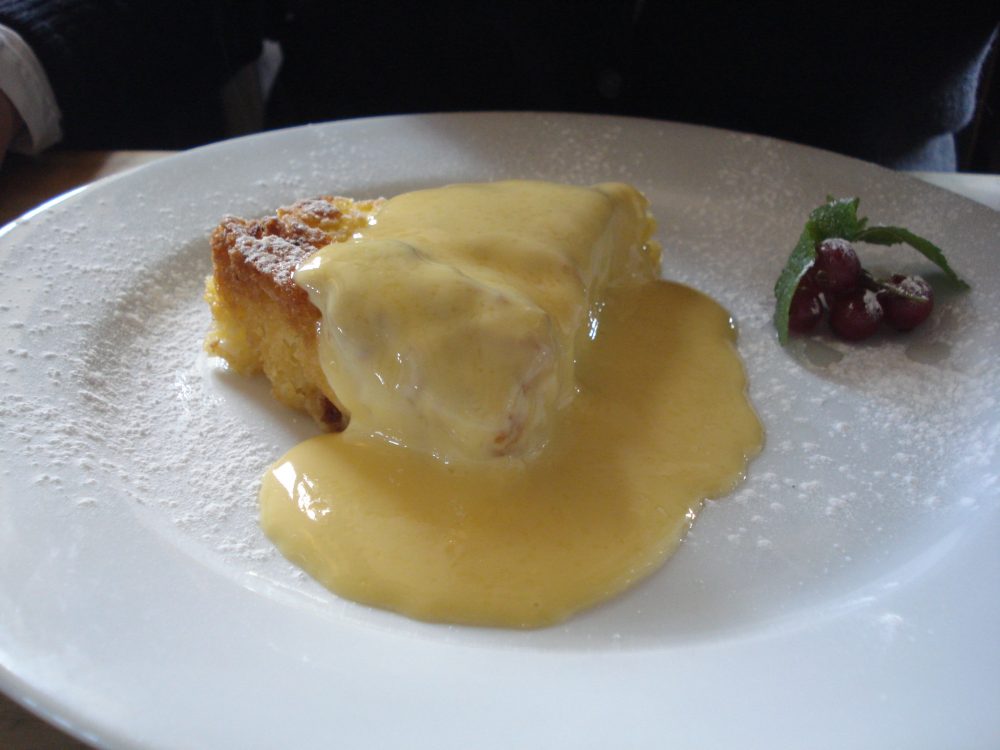 Slice of apple cake on white plate with custard on top.